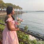 girl stanning next to the shore with a long pink dress on hold bouquet of flowers