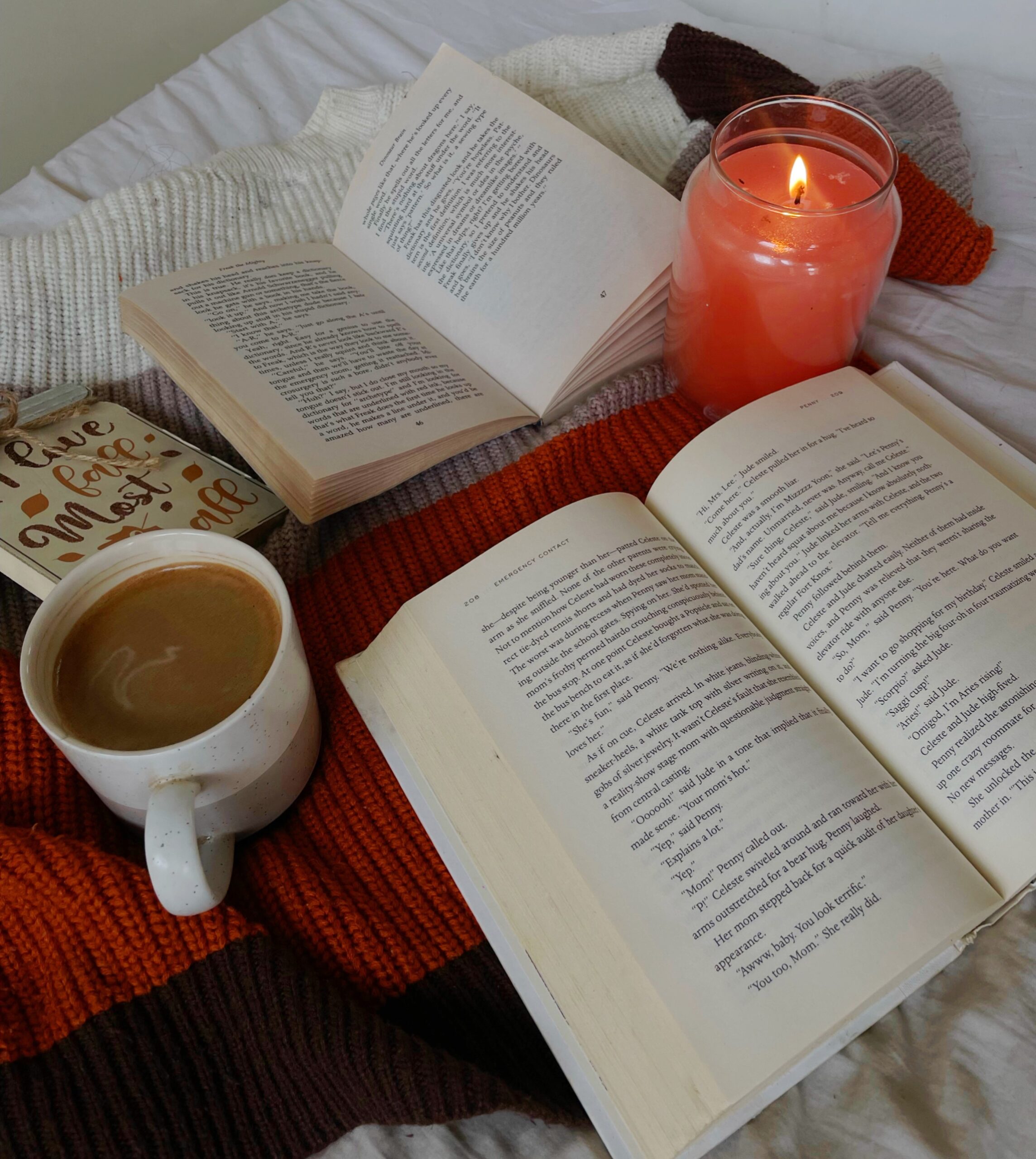 books that are open on the bed next to a cup of coffee and a lit orange candle